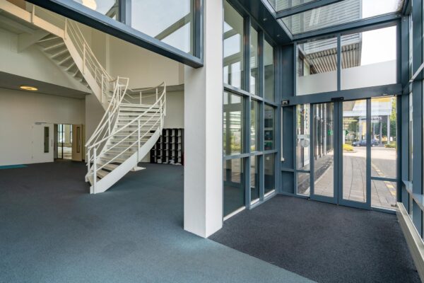 Moderne entreehal van een kantoorgebouw aan de Rivium Boulevard met glazen gevel en witte wenteltrap.